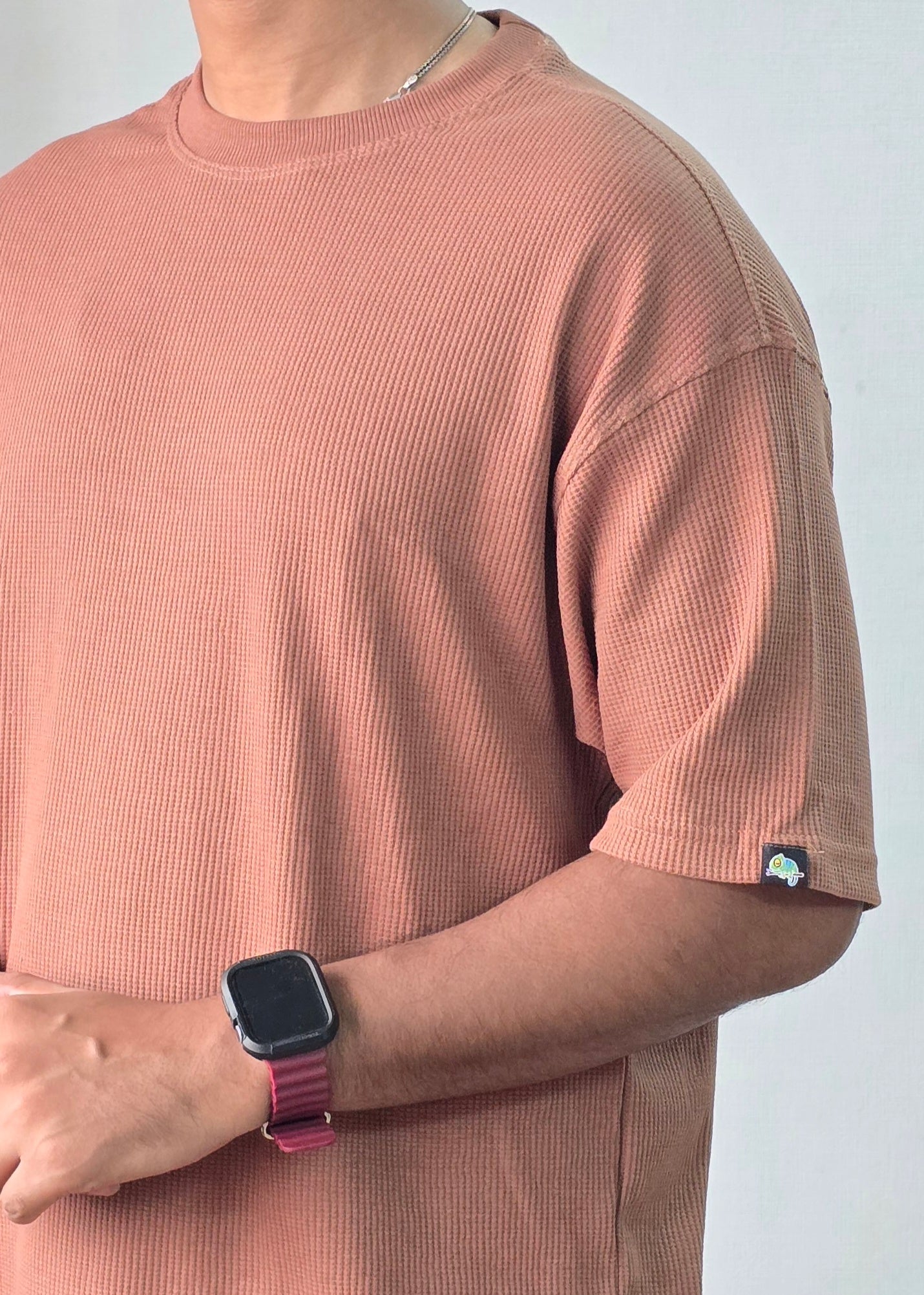 Person wearing a coffee t-shirt with a watch on a plain background
