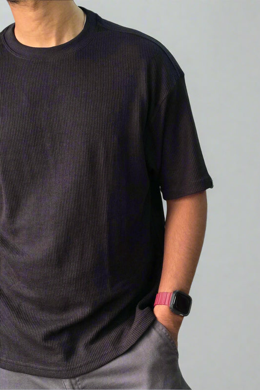 Person wearing a black t-shirt and gray pants against a plain background